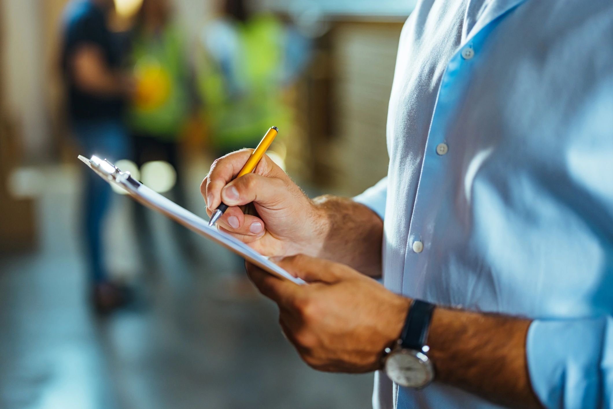 Site supervisor writing notes on a clipboard in an industrial yard